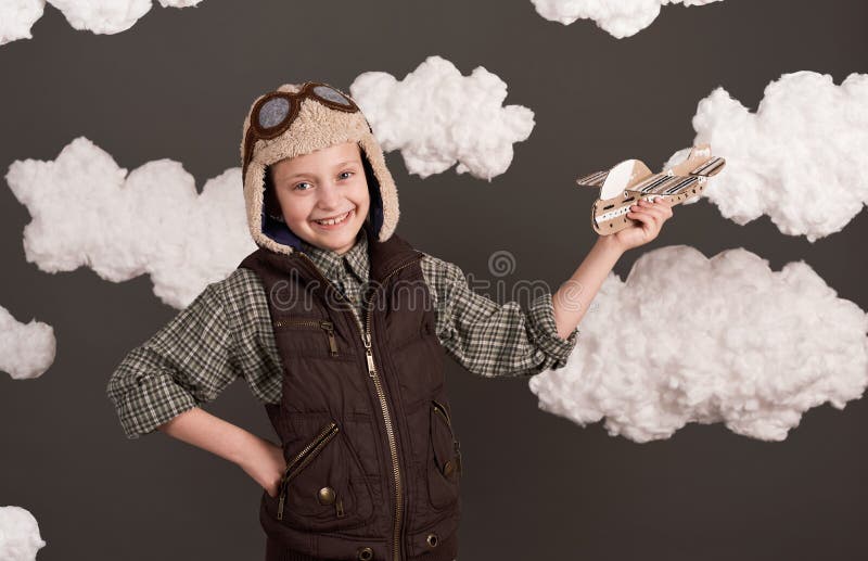 Une fille joue avec un avion en carton et des rêves de devenir un pilote vêtu d'une chemise rétro et casque de style avec des lune photographie stock libre de droits