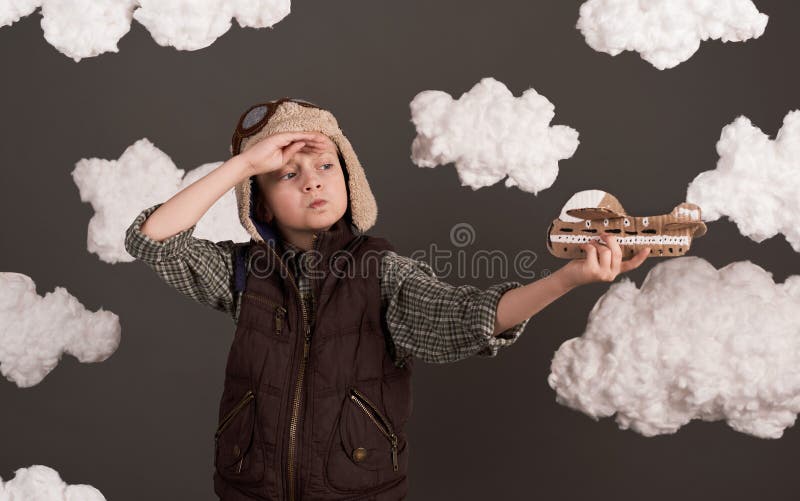 Une fille joue avec un avion en carton et des rêves de devenir un pilote vêtu d'une chemise rétro et casque de style avec des lune image stock