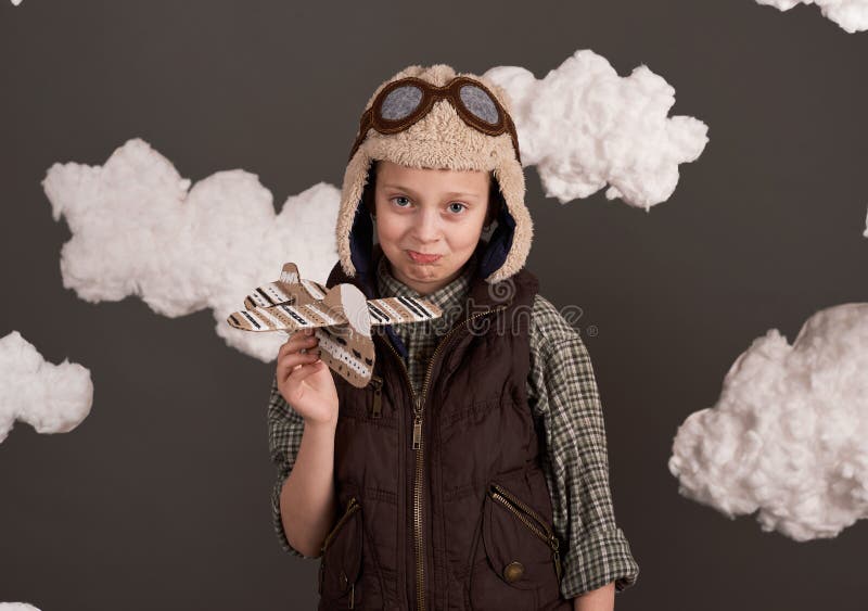 Une fille joue avec un avion en carton et des rêves de devenir un pilote vêtu d'une chemise rétro et casque de style avec des lune photos stock