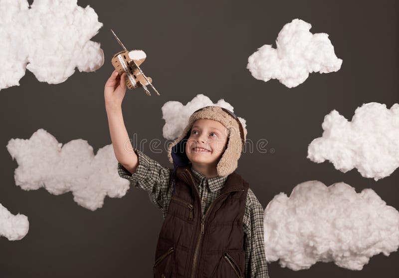 Une fille joue avec un avion en carton et des rêves de devenir un pilote vêtu d'une chemise rétro et casque de style avec des lune images stock
