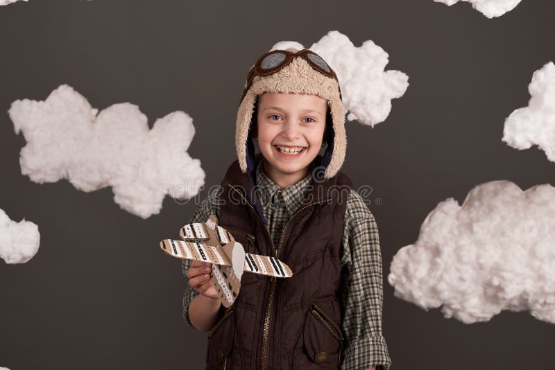Une fille joue avec un avion en carton et des rêves de devenir un pilote vêtu d'une chemise rétro et casque de style avec des lune image stock