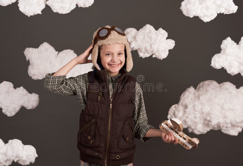 Une fille joue avec un avion en carton et des rêves de devenir un pilote vêtu d'une chemise rétro et casque de style avec des lune photographie stock