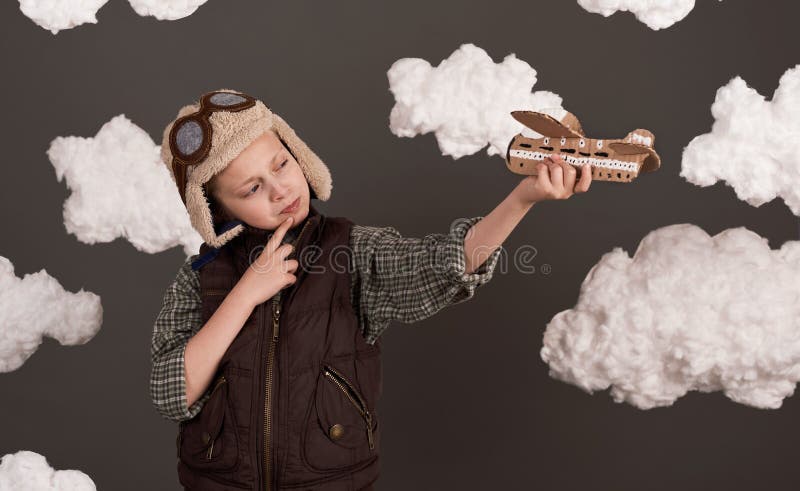 Une fille joue avec un avion en carton et des rêves de devenir un pilote vêtu d'une chemise rétro et casque de style avec des lune photographie stock
