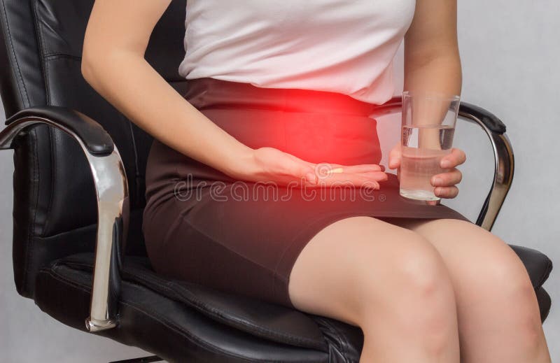 Une fille s'assied dans une chaise de bureau et tient une pilule pour la douleur dans les règles, affaires, plan rapproché, anti- photo stock Une fille s'assied dans une chaise de bureau et tient une pilule pour la douleur dans les règles, affaires, plan rapproché, anti- photo stock