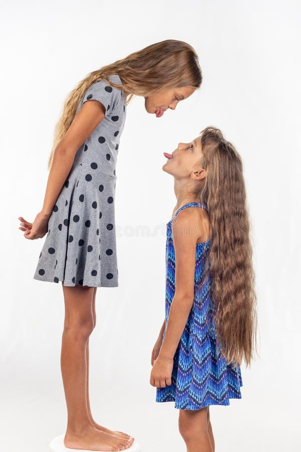 Une fille se tient sur une chaise, une autre fille se tient voisine, se montrent des langues images libres de droits Une fille se tient sur une chaise, une autre fille se tient voisine, se montrent des langues images libres de droits