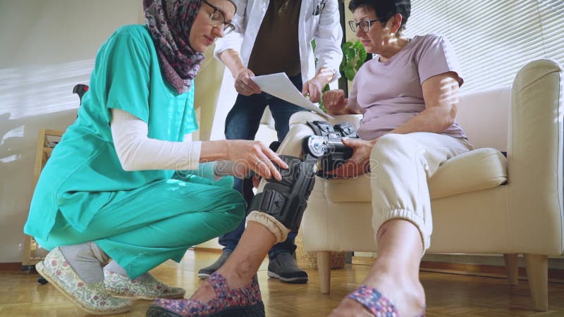 Une infirmière aide à mettre une servitude sur la jambe d'une patiente âgée banque de vidéos