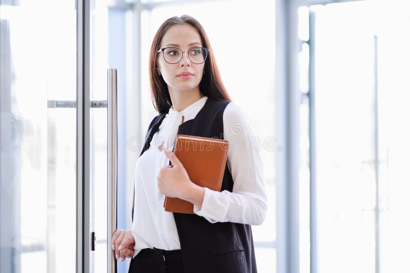 Une jeune belle fille dans des lunettes entre dans la porte en verre de bureau photo libre de droits Une jeune belle fille dans des lunettes entre dans la porte en verre de bureau photo libre de droits