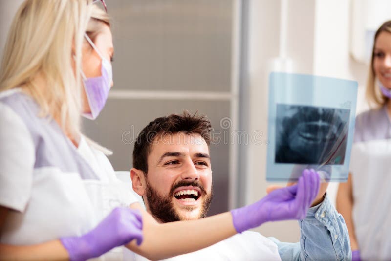 Une jeune dentiste montre une image radiologique à un jeune homme heureux image libre de droits Une jeune dentiste montre une image radiologique à un jeune homme heureux image libre de droits