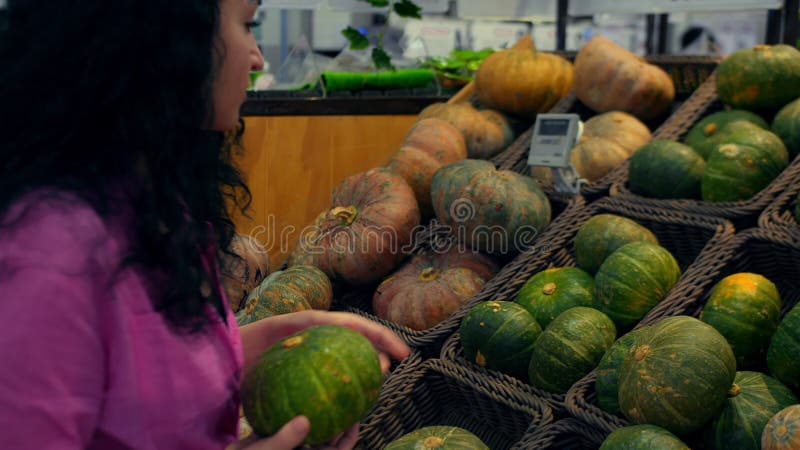 Une jeune femme achète des épiceries choisit une citrouille dans le supermarché pour un séjour vide. jolie jeune fille rose banque de vidéos