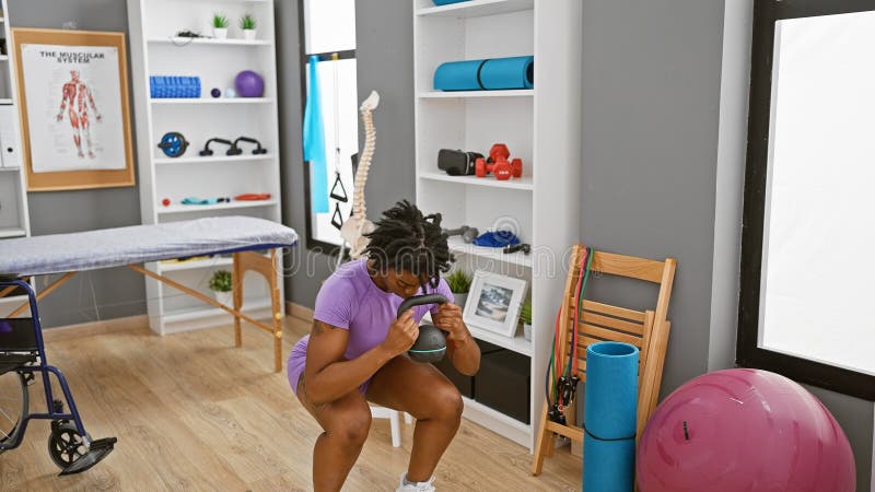 Une jeune femme afro-américaine avec des exercices de dreadlocks dans une clinique de désintoxication à l'aide d'une kettlebell photo stock