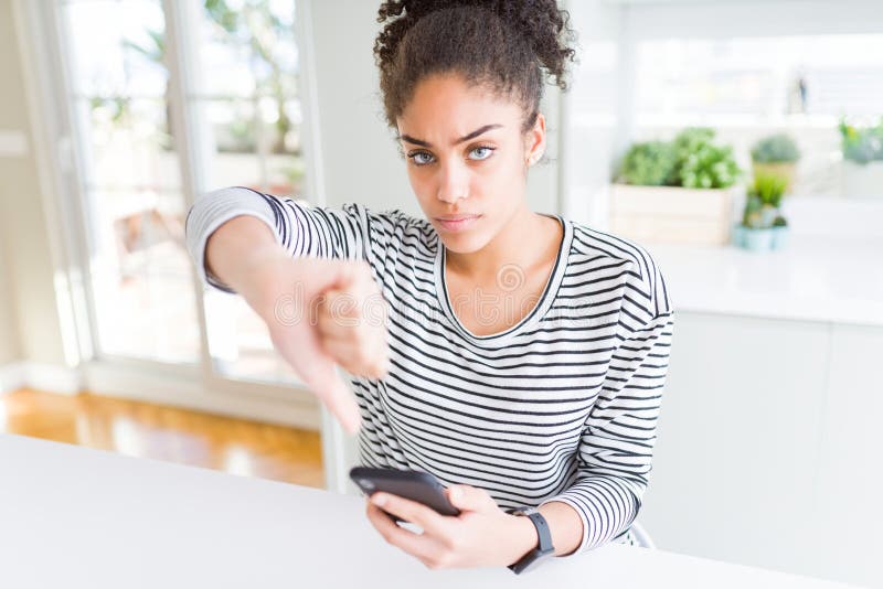 Une jeune femme afro-américaine utilisant un smartphone envoyant un message avec un visage en colère signe négatif montrant son av image libre de droits