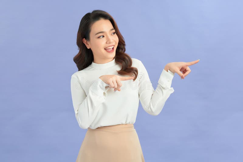 Une jeune femme asiatique fait un geste deux doigts pointés latéralement au-dessus de présenter le produit quelque chose photographie stock