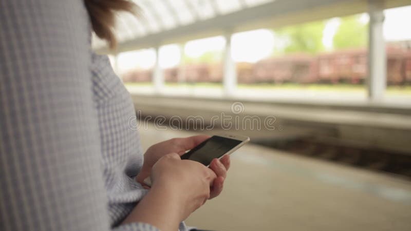 Une jeune femme assise sur un banc. gare. la jeune fille écrit un message sur le téléphone utilise internet en attendant clips vidéos