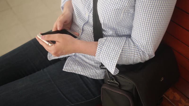Une jeune femme assise sur un banc. gare. la jeune fille écrit un message sur le téléphone utilise internet en attendant banque de vidéos
