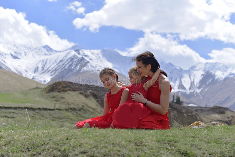 Une jeune femme avec deux filles dans des robes rouges se reposant dans les montagnes couronn?es de neige au printemps photographie stock Une jeune femme avec deux filles dans des robes rouges se reposant dans les montagnes couronn?es de neige au printemps photographie stock