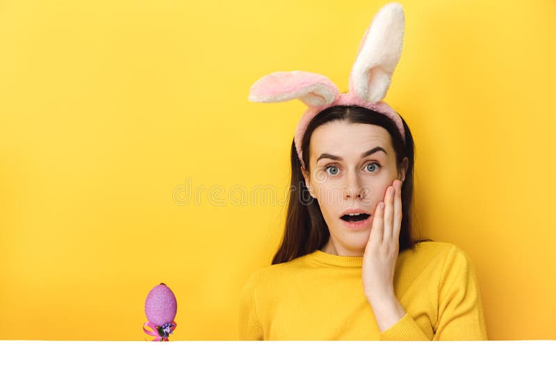 Une jeune femme choquée avec des oreilles moelleuses lapin et un oeuf de pâques pourpre apprécie les traditions de fête habillé en photos stock