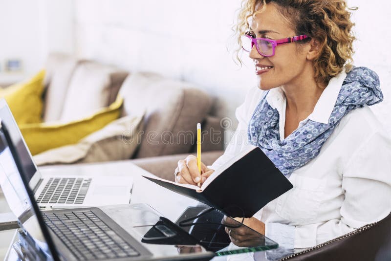Une jeune femme d'affaires sourit et travaille avec deux ordinateurs portables différents - un bureau moderne alternatif à la mai photographie stock