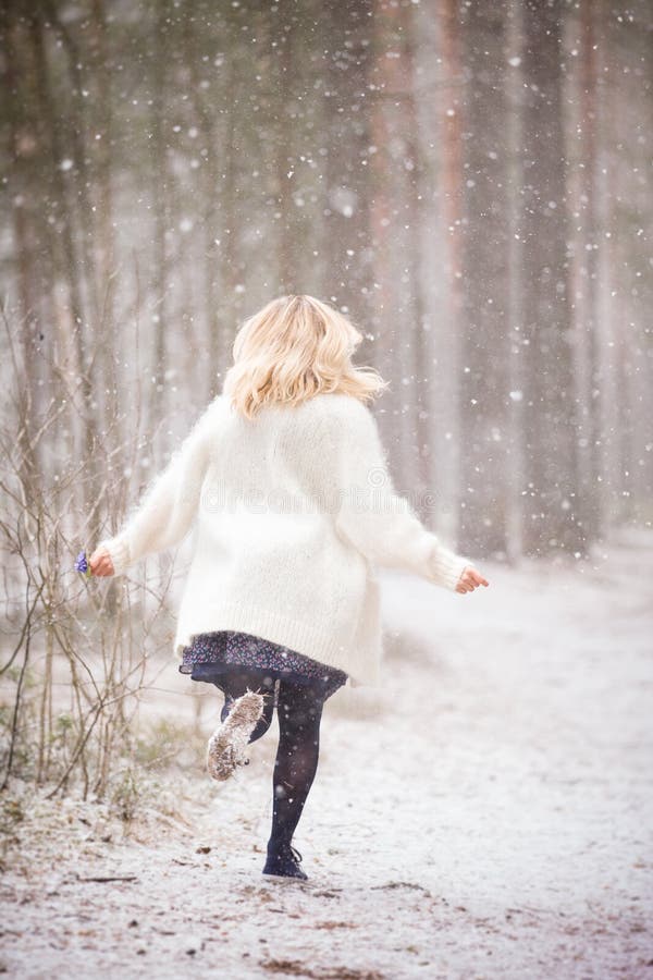 Une jeune femme dans un cardigan chaud blanc fonctionnant dans une forêt et tenant un groupe de premières fleurs de bleu de resso photographie stock Une jeune femme dans un cardigan chaud blanc fonctionnant dans une forêt et tenant un groupe de premières fleurs de bleu de resso photographie stock
