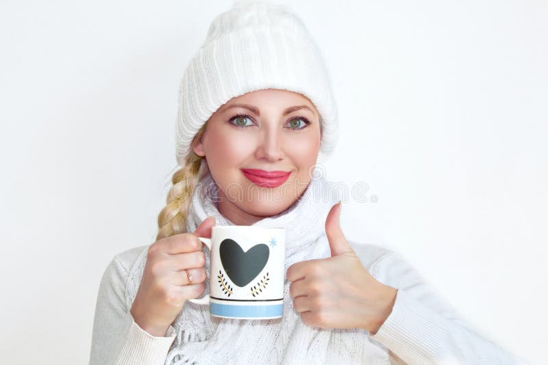 Une jeune femme dans un chapeau et une écharpe tricotés tenant une tasse de thé et montrant son pouce photos libres de droits Une jeune femme dans un chapeau et une écharpe tricotés tenant une tasse de thé et montrant son pouce photos libres de droits