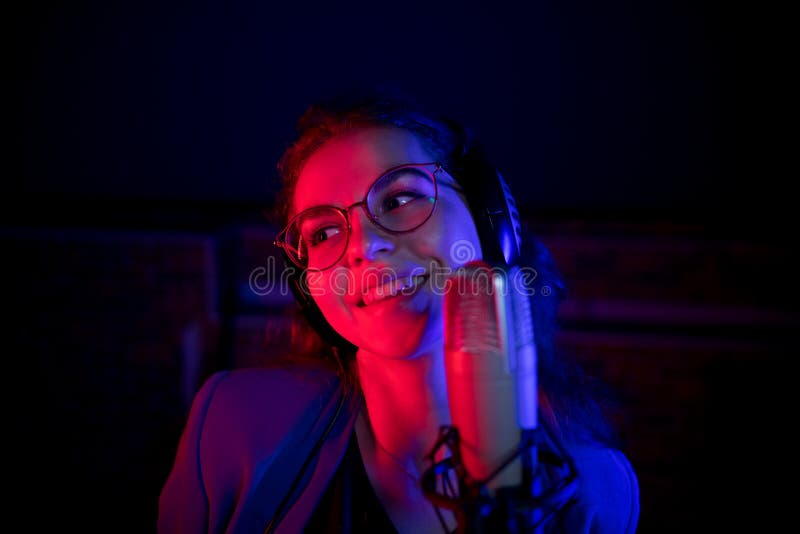 Une jeune femme de sourire en verres chantant par le microphone dans l'?clairage au n?on photographie stock Une jeune femme de sourire en verres chantant par le microphone dans l'?clairage au n?on photographie stock