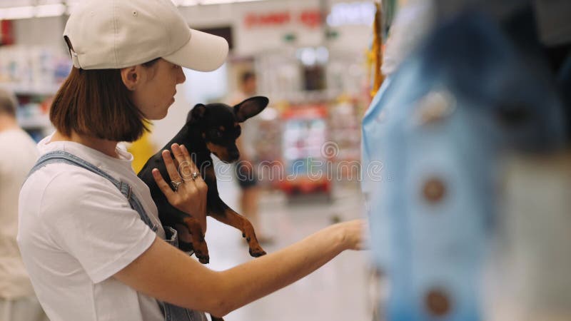 Une jeune femme faisant ses courses au supermarché avec un petit chien dans les mains.