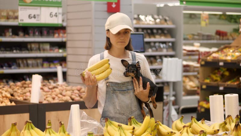 Une jeune femme faisant ses courses au supermarché avec un petit chien dans les mains.