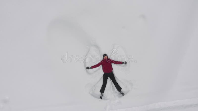 Une jeune femme fait un ange de neige dans la neige, vue sur le dessus du drone, rotation banque de vidéos