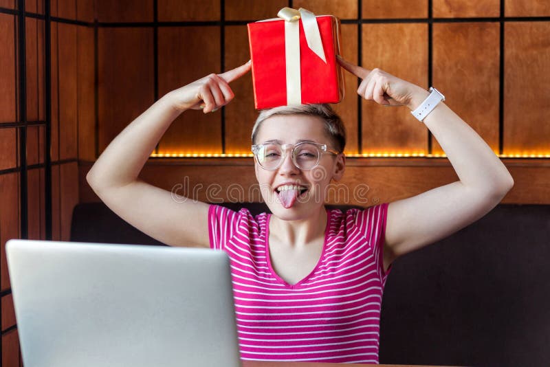 Une jeune femme heureuse et chilienne aux cheveux courts en t-shirt rose et lunettes est assise dans un café, tenant une boîte ro image stock