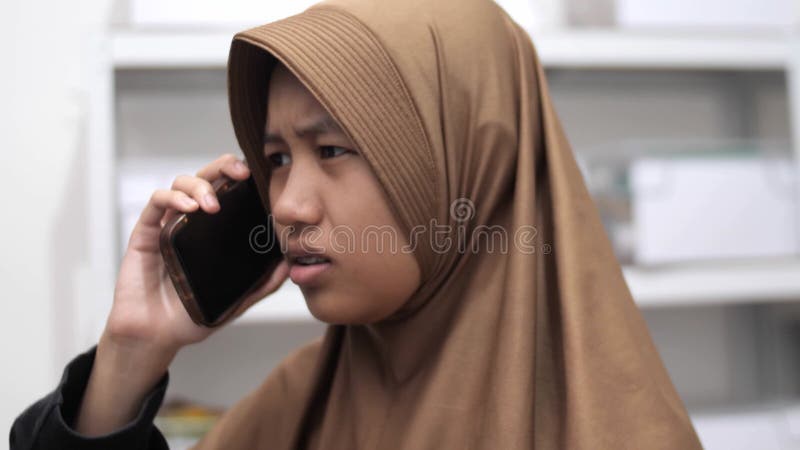 Une jeune femme musulmane d'asie a l'air confuse et contrariée quand elle parle au téléphone et reçoit de mauvaises nouvelles clips vidéos