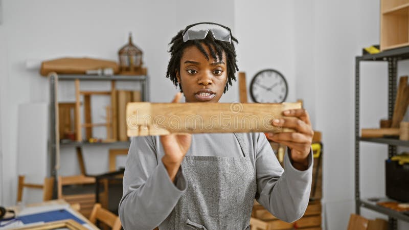 Une jeune femme noire ciblée examine un morceau de bois dans un atelier de menuiserie images libres de droits
