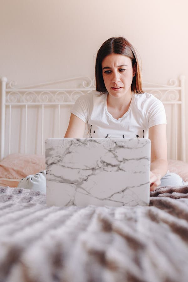 Une jeune femme qui utilise un ordinateur portable à la maison, un visage sérieux et qui pense à la confusion images stock Une jeune femme qui utilise un ordinateur portable à la maison, un visage sérieux et qui pense à la confusion images stock
