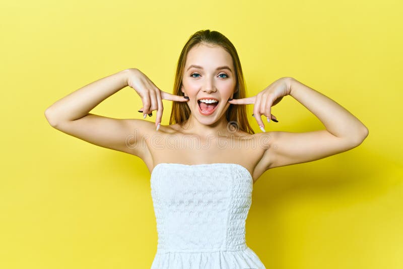 Young woman laughing at camera, making funny faces during photosoot. Studio shot of pretty blond girl fooling around on bright yellow background. Young woman laughing at camera, making funny faces during photosoot. Studio shot of pretty blond girl fooling around on bright yellow background