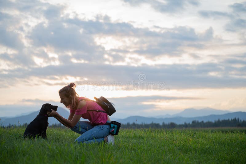 Une jeune femme s'agenouillant pour agiter son mignon chiot noir labrador image libre de droits