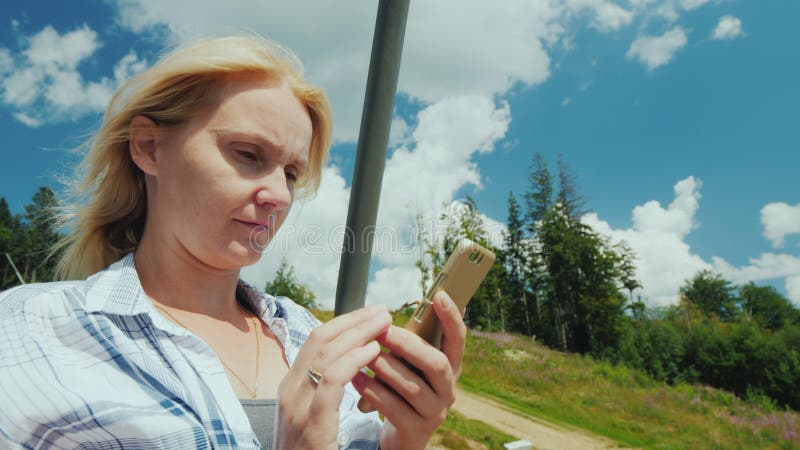 Une jeune femme utilise un smartphone, monte un remonte-pente un jour clair d'été