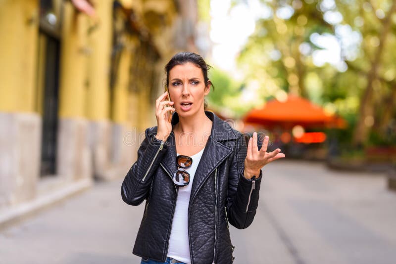 Une jeune femme étant dérangée tout en à l'aide de son téléphone dans un envir urbain images stock Une jeune femme étant dérangée tout en à l'aide de son téléphone dans un envir urbain images stock