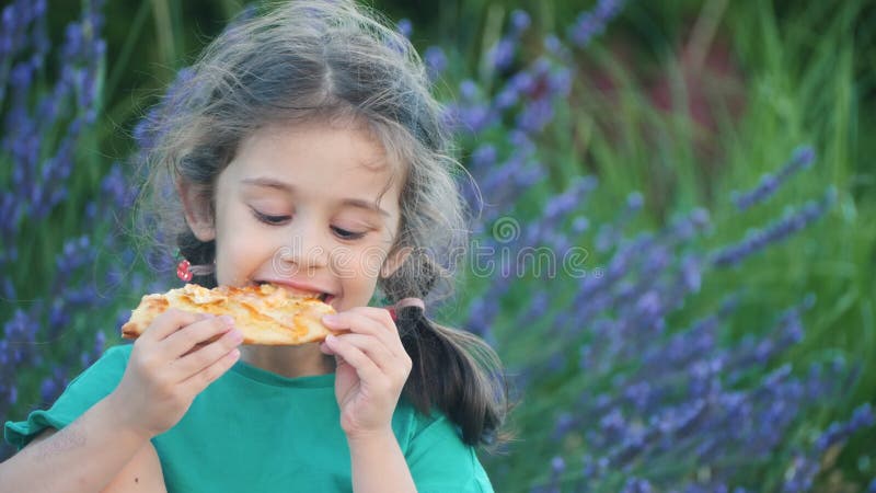 Une jeune fille aime manger une part de pizza à l'extérieur entourée de fleurs de lavande vibrantes dans un naturel serein clips vidéos