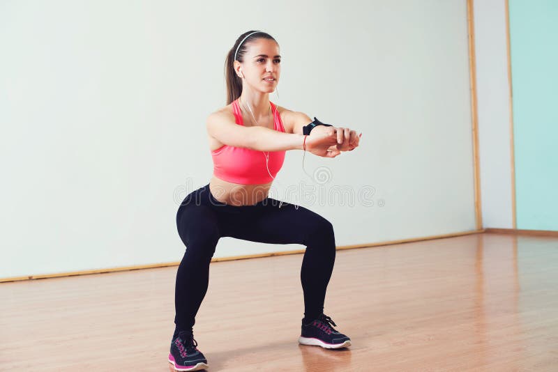 Une jeune fille faisant des postures accroupies dans un gymnase Jeune femme dans l'usage de sport avec la séance d'entraînement d photos stock