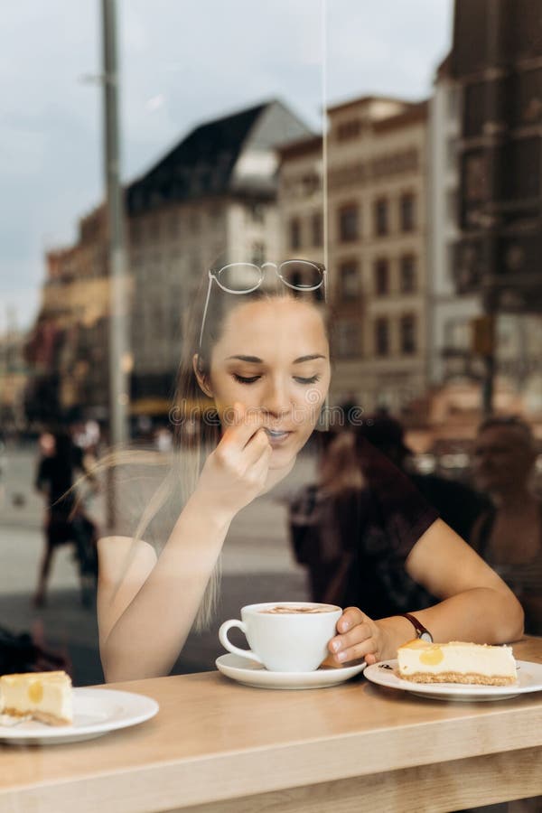 Une jeune fille mange un gâteau et boit du café dans un café photographie stock Une jeune fille mange un gâteau et boit du café dans un café photographie stock