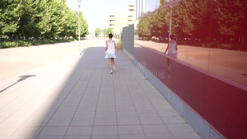 Une jeune fille marche joyeusement à travers un environnement urbain ensoleillé rempli d'excitation banque de vidéos