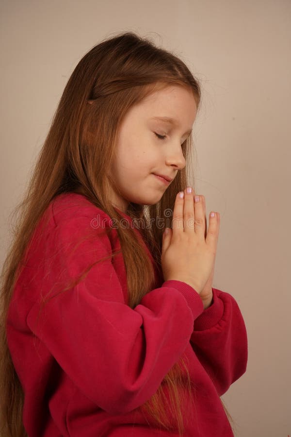 Une jeune fille serre doucement ses mains ensemble comme dans la prière. Son expression sereine reflète l'innocence et la paix. A. Un moment émouvant rempli de pureté et de dévotion.