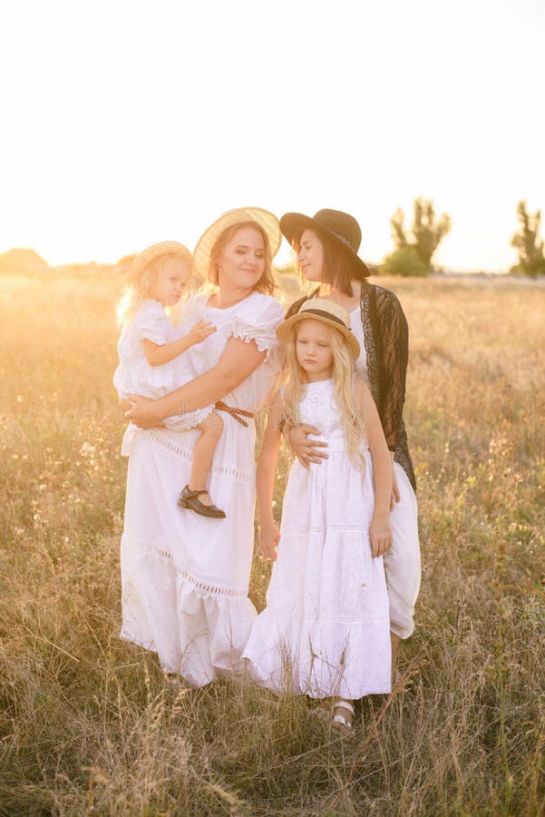 Une jeune mère avec ses filles et une tante avec les cheveux blonds dans des robes blanches au coucher du soleil pendant l'été da images libres de droits Une jeune mère avec ses filles et une tante avec les cheveux blonds dans des robes blanches au coucher du soleil pendant l'été da images libres de droits