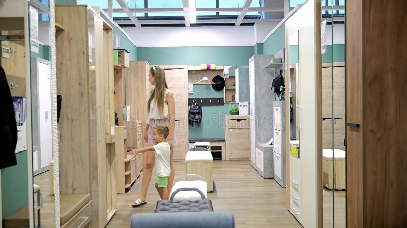 Une jeune mère avec son fils de 3 ans dans un magasin de meubles choisit un nouveau couloir. achat de mobilier moderne pour banque de vidéos