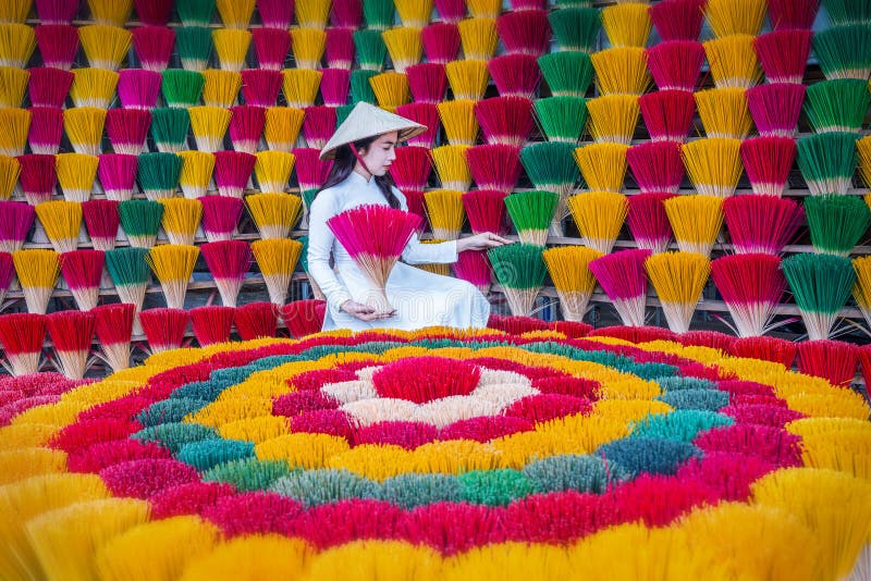 Une jeune vietnamienne en costume blanc national met en place des bâtons d'encens colorés en teinte vietnam photos libres de droits