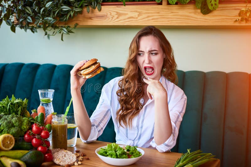 Une jolie femme refuse de manger un hamburger malsain Elle le regarde avec dégoût photo libre de droits Une jolie femme refuse de manger un hamburger malsain Elle le regarde avec dégoût photo libre de droits