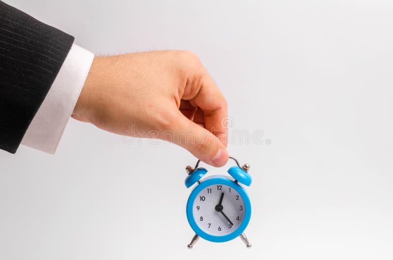 Une main du ` s d'homme d'affaires tient un réveil bleu sur un fond blanc Le concept de l'écoulement du temps, temps à l'action S photos libres de droits Une main du ` s d'homme d'affaires tient un réveil bleu sur un fond blanc Le concept de l'écoulement du temps, temps à l'action S photos libres de droits