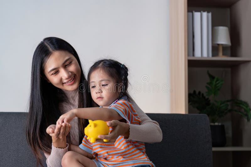 Une mère diversifiée enseignant à sa fille à économiser de l'argent avec une tirelire jaune à la maison favorisant l'alphabétisati image stock