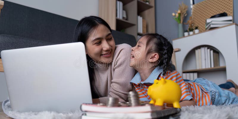 Une mère et une fille diverses partagent le rire tout en économisant de l'argent avec la tirelire jaune et l'ordinateur portable à photos libres de droits