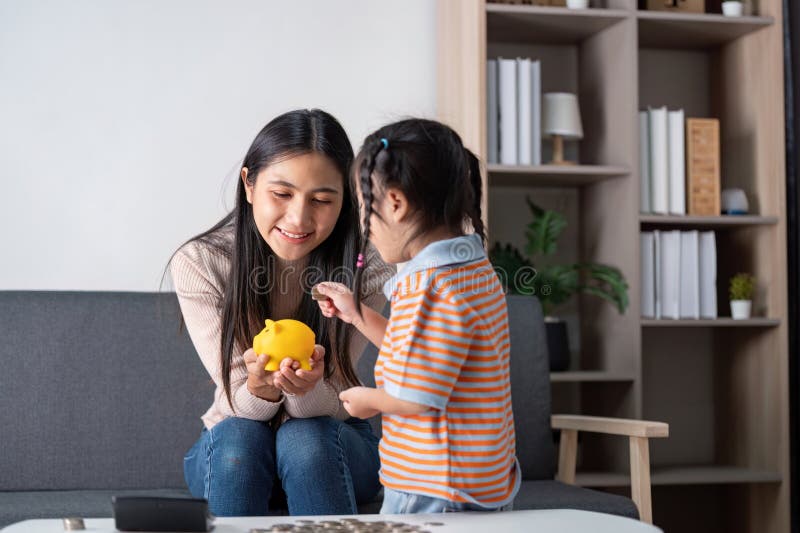 Une mère et une fille diversifiées explorant l'épargne avec une tirelire jaune à la maison promouvoir l'éducation financière et fa images stock