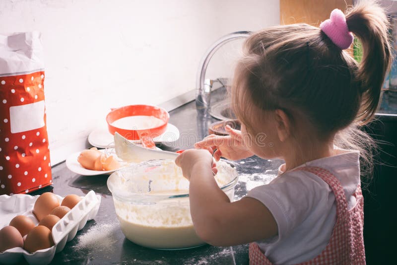 Une petite fille mignonne préparant la pâte dans la cuisine à la maison photographie stock Une petite fille mignonne préparant la pâte dans la cuisine à la maison photographie stock