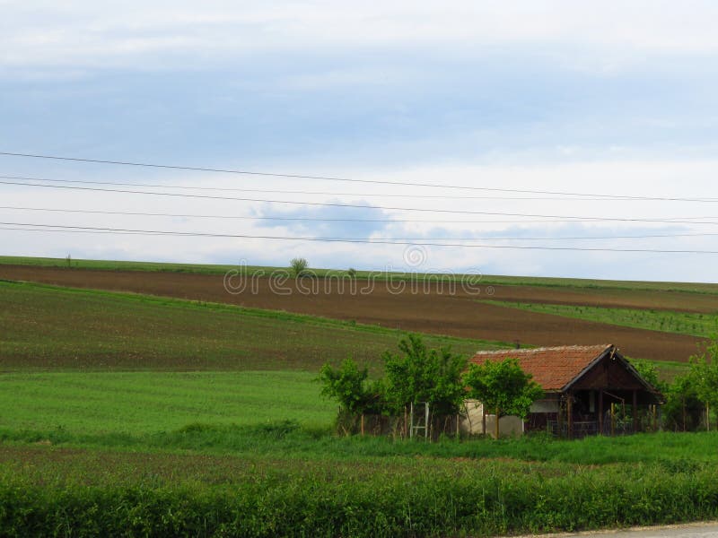 Une petite maison entourée par l'herbe verte de champ et le champ labouré Ploughed a cultivé la terre image stock Une petite maison entourée par l'herbe verte de champ et le champ labouré Ploughed a cultivé la terre image stock